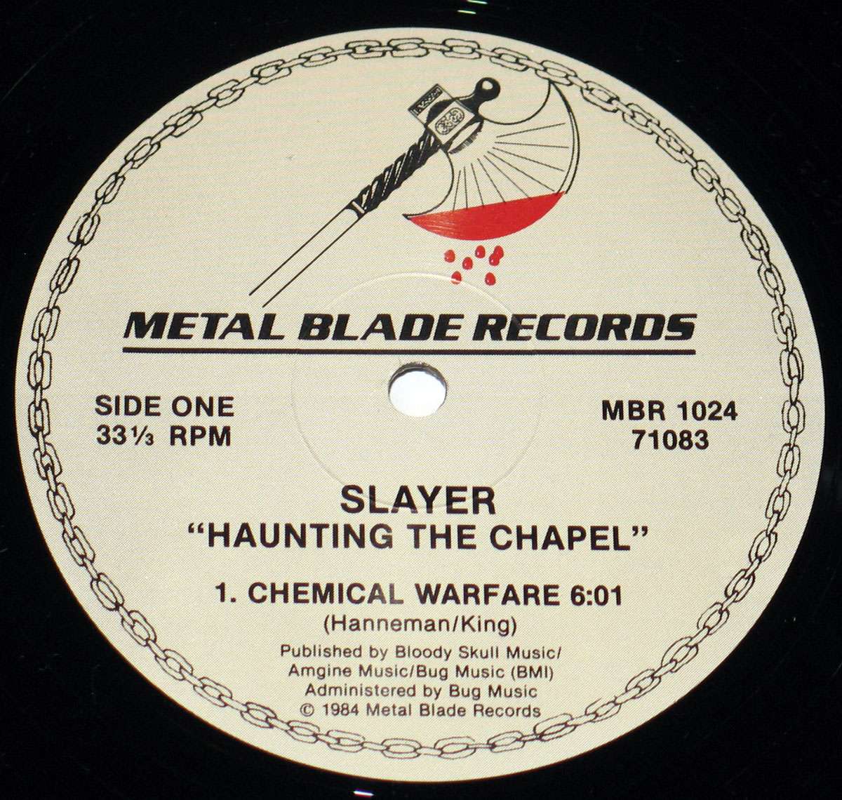 Close-up of Side One label of Slayer's 'Haunting the Chapel' vinyl record. Features Metal Blade Records logo with a blood-dripping axe, a chain border, and black printed text displaying track details, including 'Chemical Warfare' by Hanneman/King.